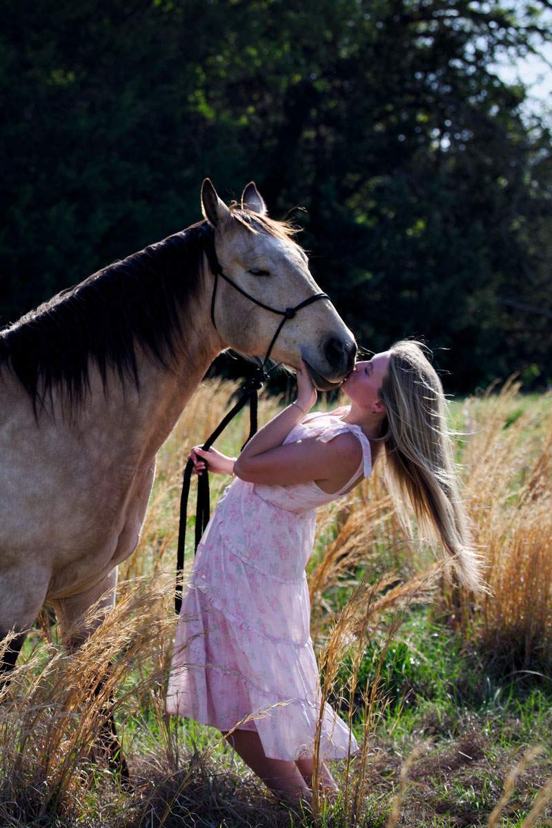 Young woman in a pink dress sharing a quiet moment with her horse in a sunlit Texas pasture