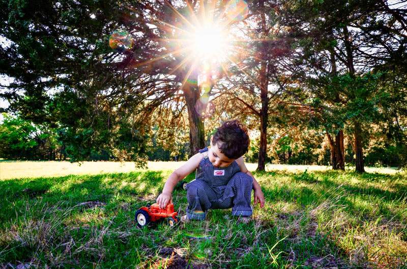 Toddler playing with a vintage red toy tractor under sunlit trees — family session in Greenville, Texas