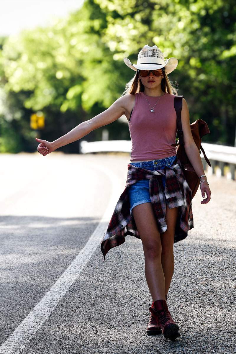 Senior portrait of a young woman in a cowboy hat and denim shorts walking a Texas country road