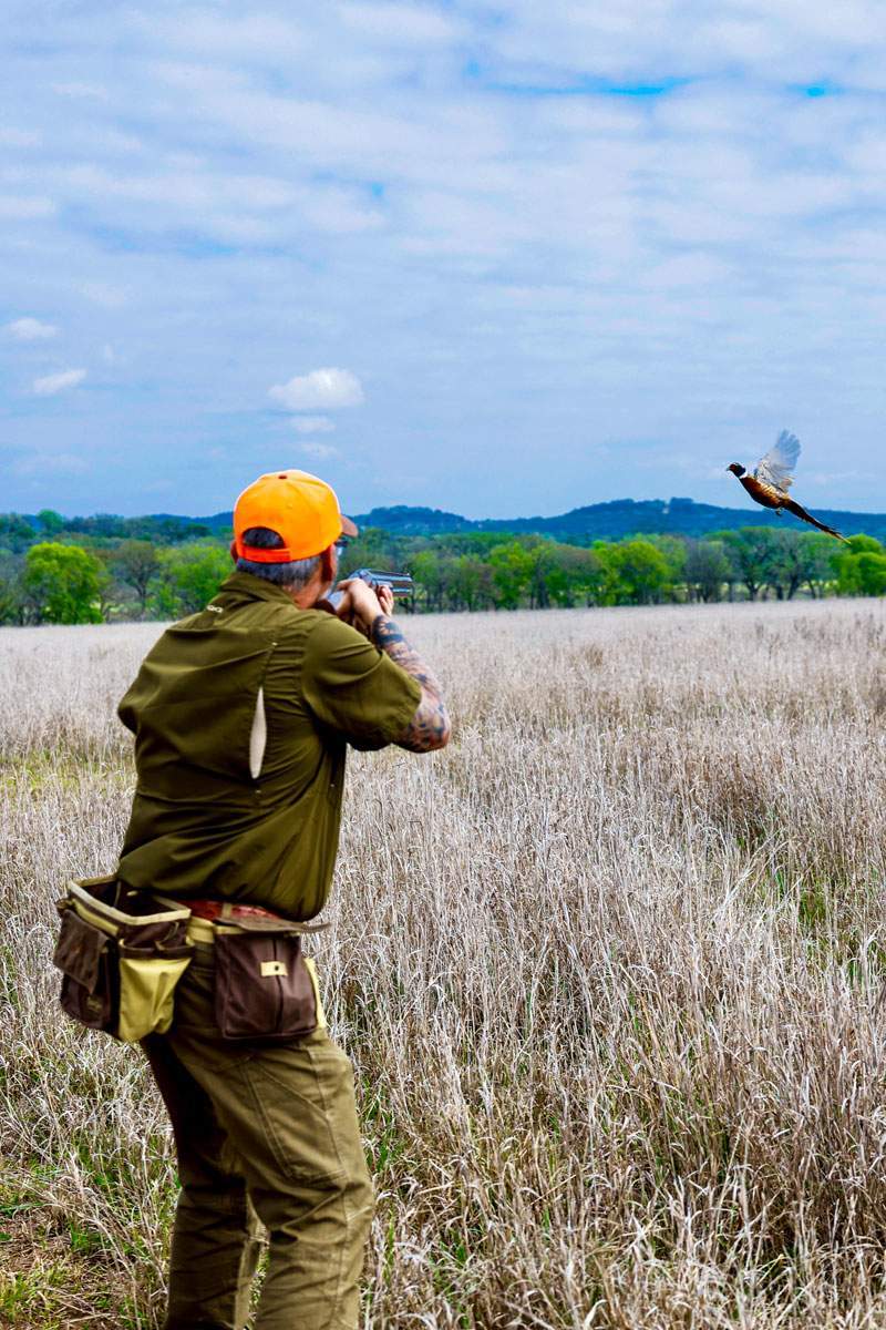Upland bird hunter taking aim at a rising pheasant over a Texas prairie — outdoor lifestyle session